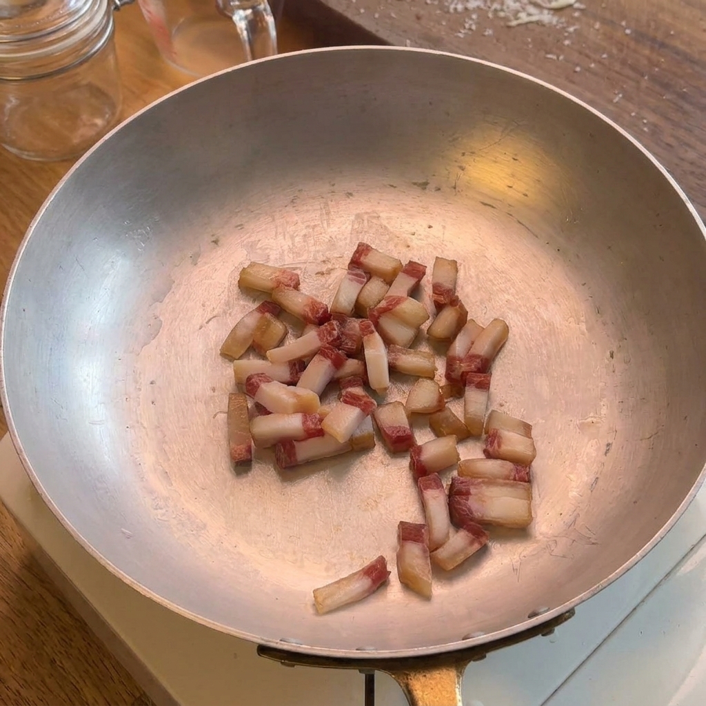 Cubetti di guanciale che friggono in una padella dacciaio inox, rilasciando il loro grasso naturale.