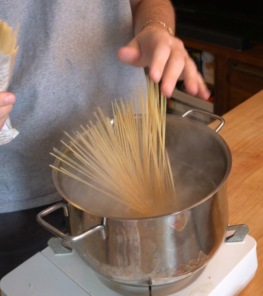 Una persona che cala un mazzo di spaghetti secchi in una pentola di acqua bollente su un fornello portatile.