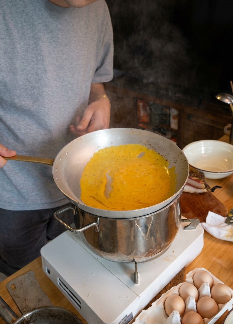 Uno chef che salta gli spaghetti in una padella sopra una pentola fumante per emulsionare la salsa.