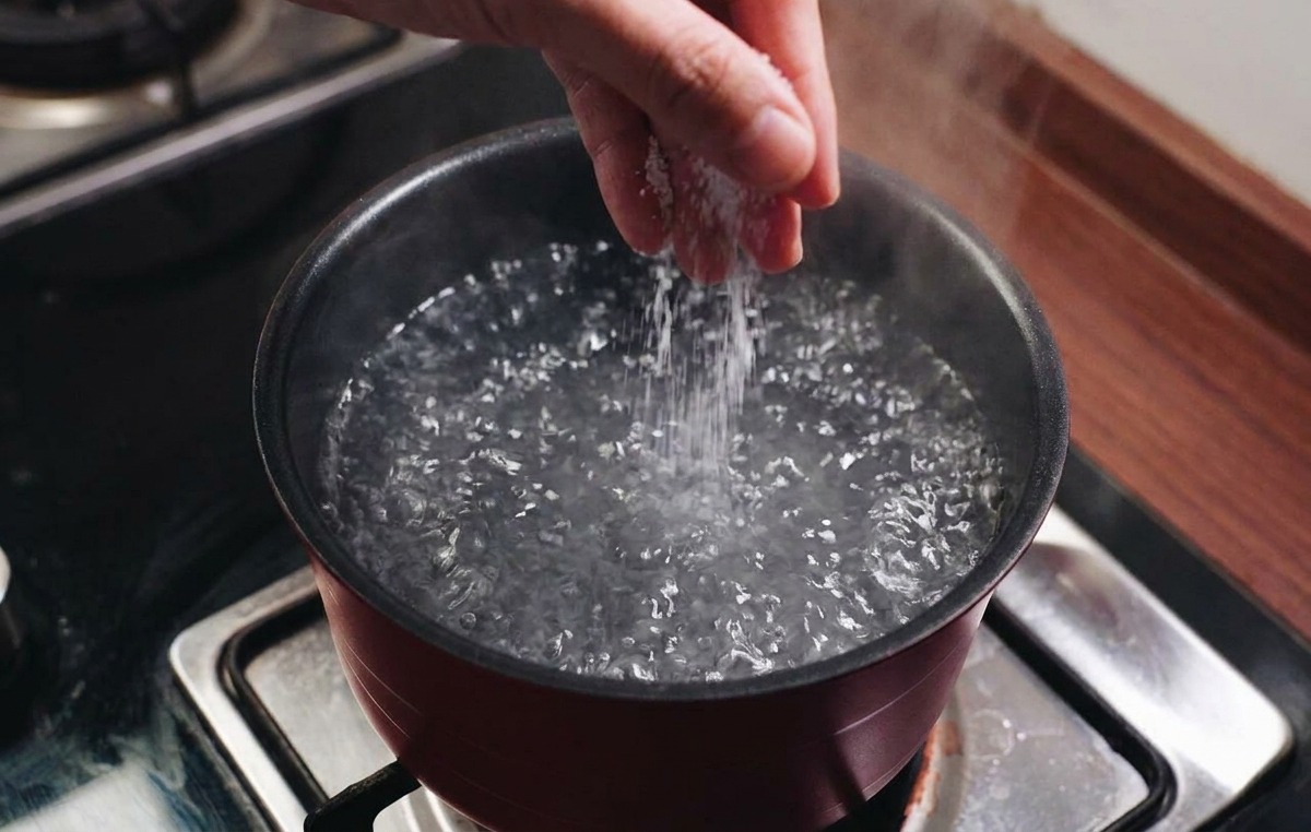 Una mano che versa il sale in una pentola di acqua che bolle vigorosamente.