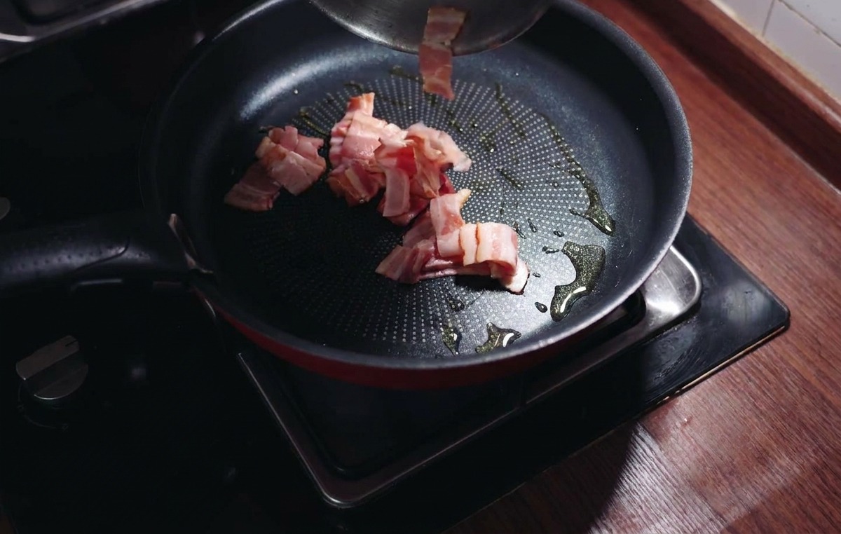 Cubetti di pancetta aggiunti in una padella calda con olio doliva lucente.