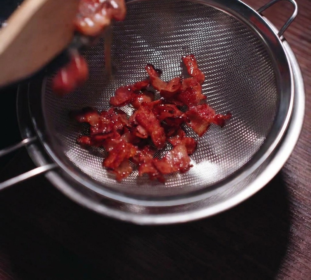 Pancetta croccante versata in un colino a maglia fine per separare il grasso liquido.