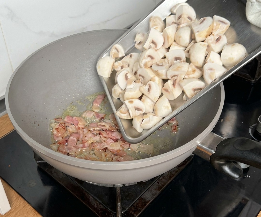 Funghi tagliati in quarti aggiunti in padella dove la pancetta sta già cuocendo.