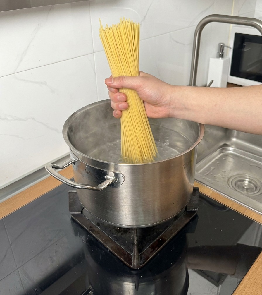 Un mazzo di spaghetti secchi immersi in una pentola dacciaio con acqua bollente.