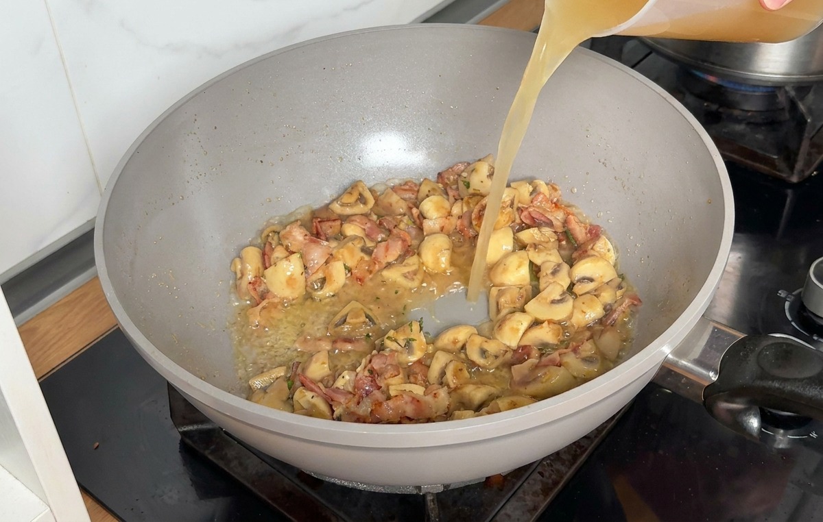 Brodo di pollo versato da un misuratore trasparente nella padella con gli ingredienti saltati.