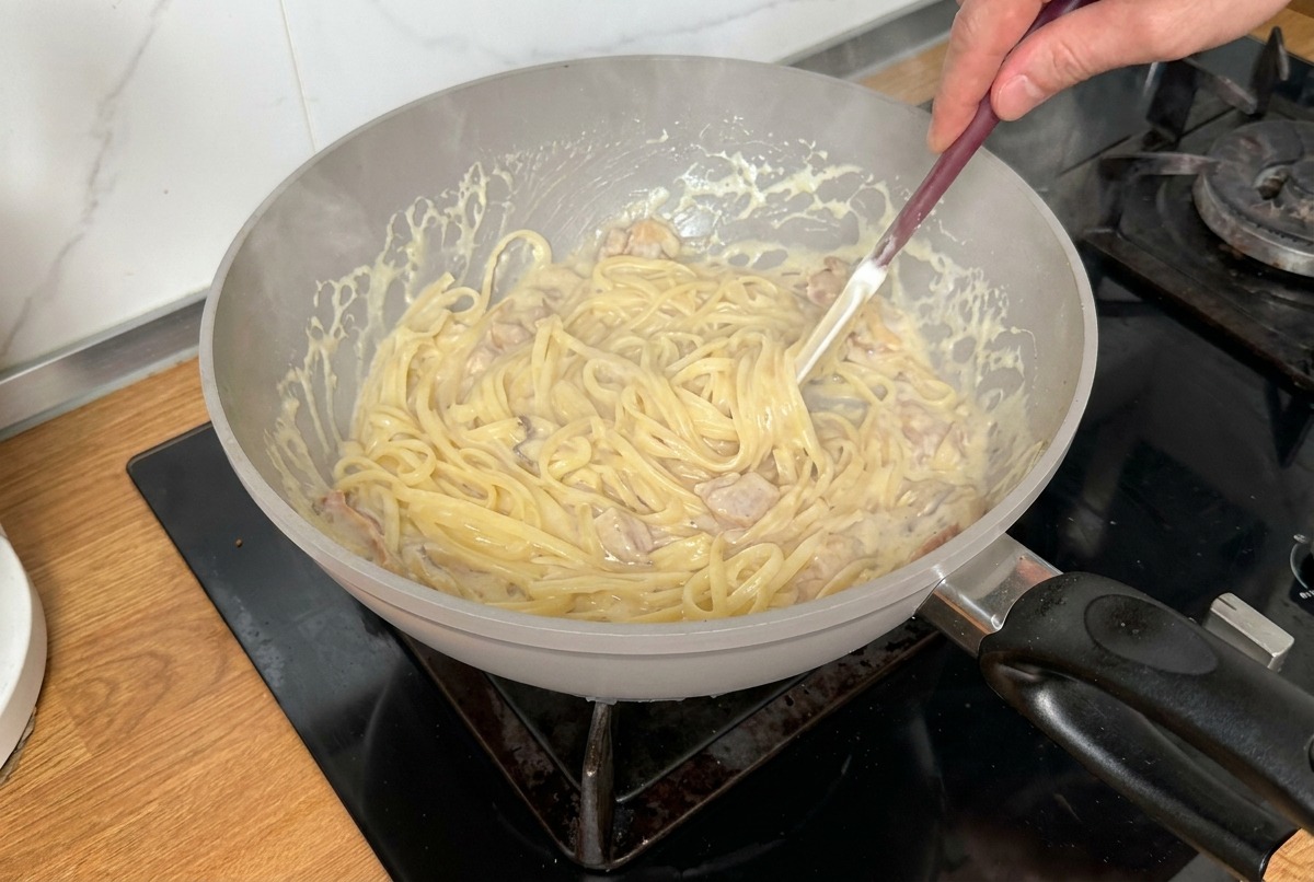 Pasta saltata e mescolata con una spatola in una salsa cremosa per garantire una copertura uniforme.