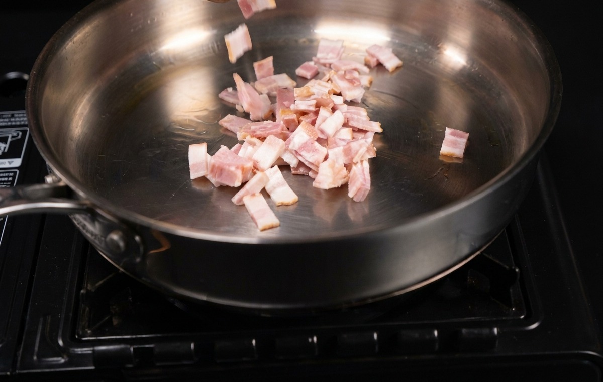 Pezzetti di pancetta che sfrigolano in una padella di acciaio inossidabile.