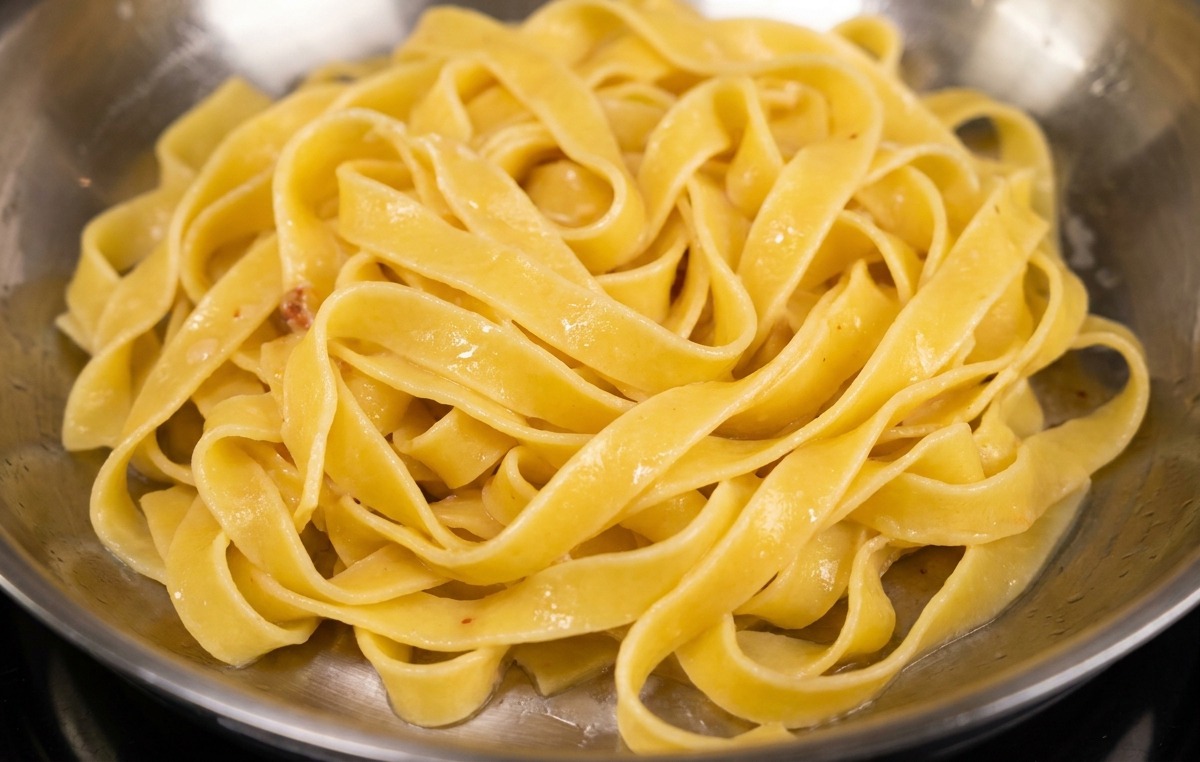 Fettuccine aggiunte nella padella con la pancetta dorata e il suo grasso saporito.