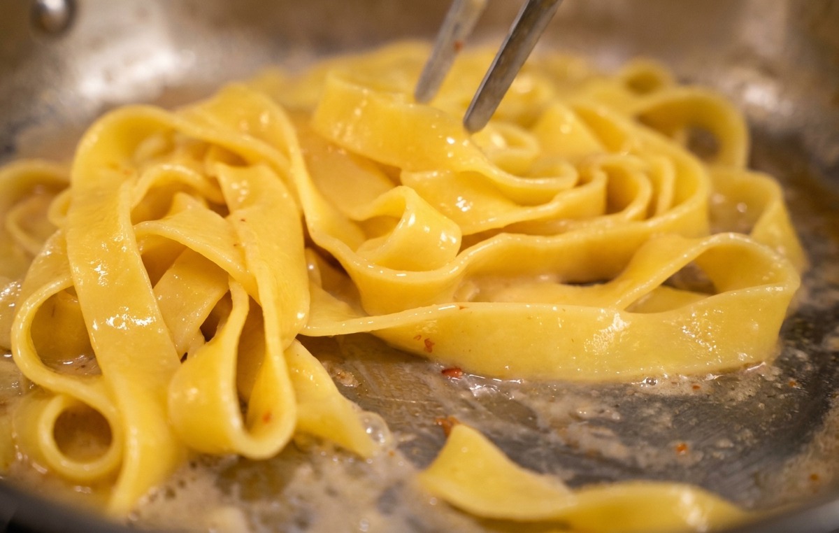 Pinze da cucina che saltano la pasta in padella per emulsionare la crema di uova e formaggio.
