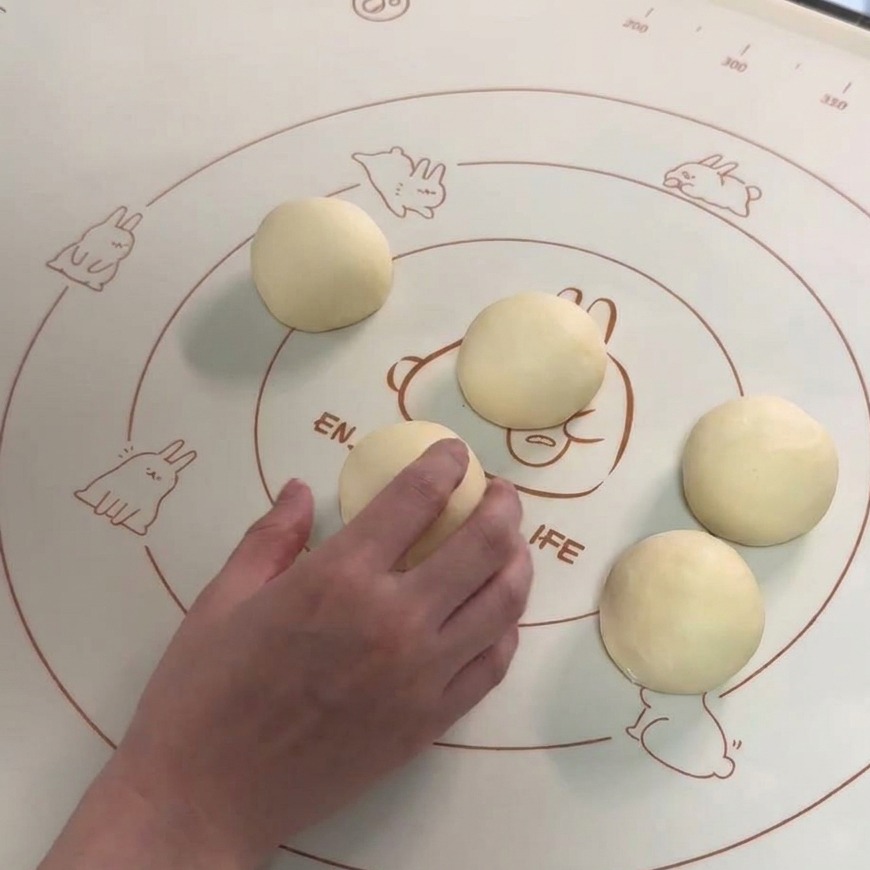 Sei palline di impasto lisce disposte su un tappetino in silicone, con una mano che ne arrotonda una.