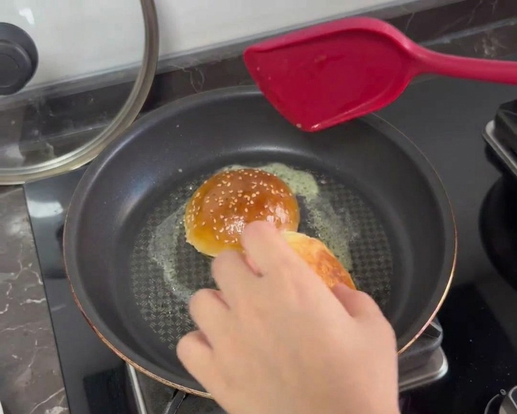 Metà dei panini per burger tostate rivolte verso il basso in una padella con burro fuso spumeggiante.