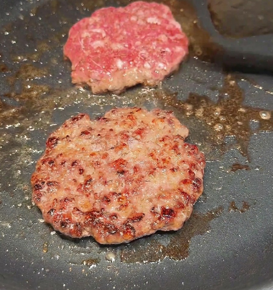 Una spatola che gira un hamburger in padella mostrando una crosticina ben rosolata e bruna.