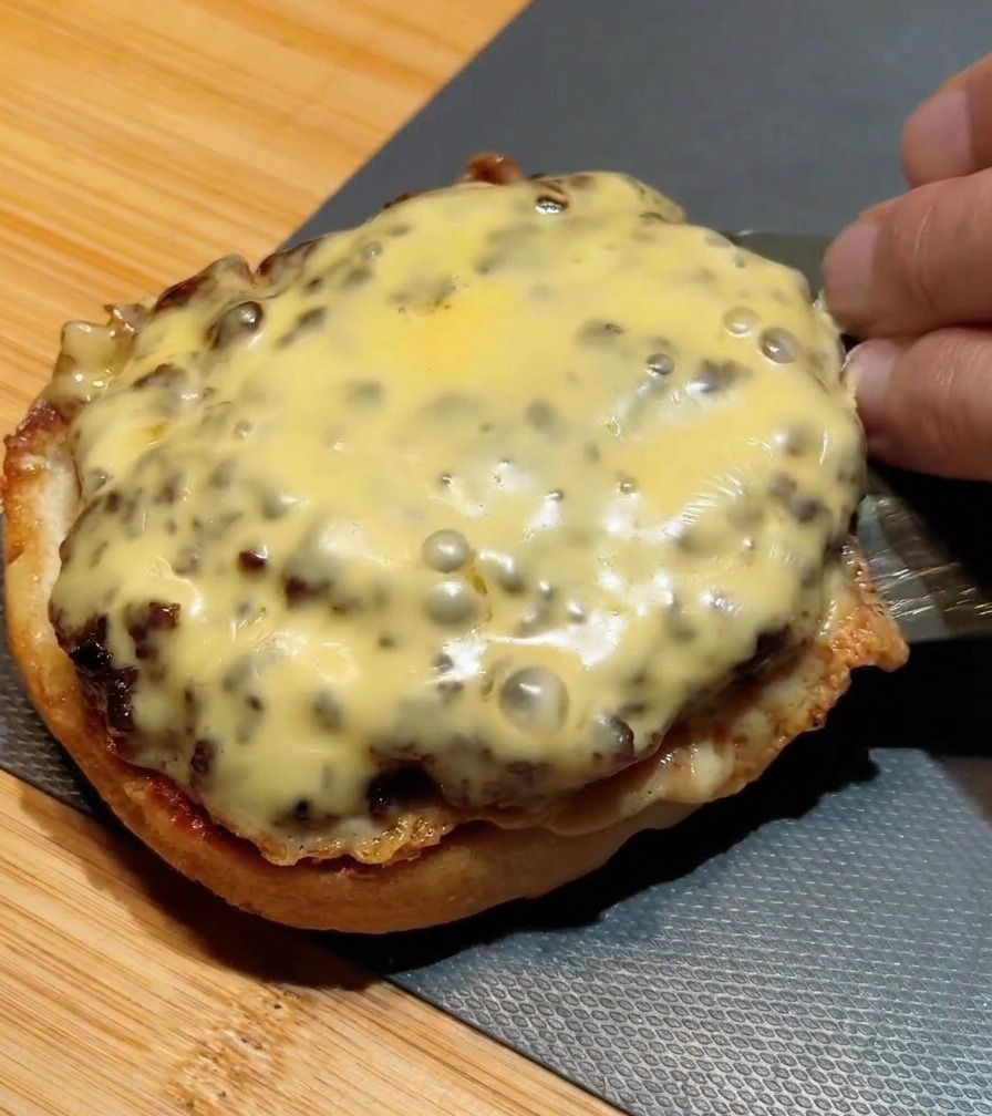 Una spatola di metallo che impila un secondo hamburger con formaggio fuso sopra quello già posizionato sul pane.
