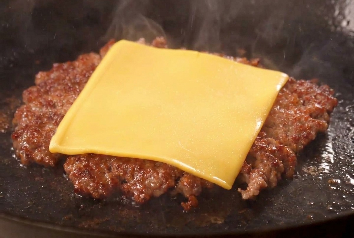 Una fetta di formaggio americano giallo che si scioglie sopra un burger di manzo ben rosolato in padella.