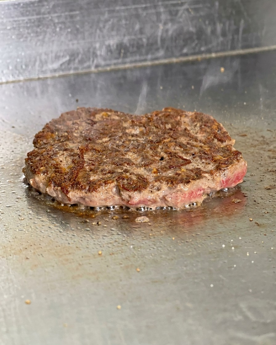 Un burger cotto e girato sulla piastra che mostra una crosticina bruna e croccante con il grasso che ribolle.
