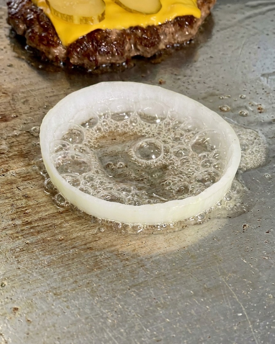Una fetta di cipolla bianca sulla piastra con un uovo crudo che frigge allinterno circondato dallolio.