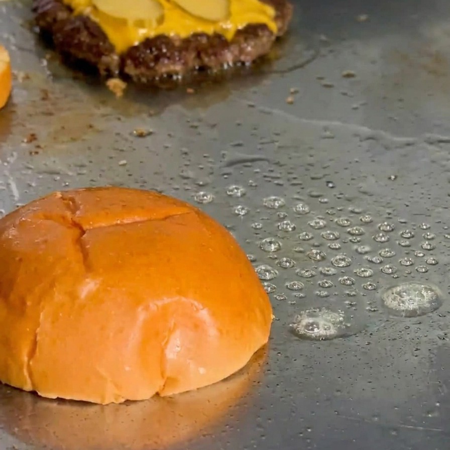 La parte superiore di un pan brioche che tosta sulla piastra con il grasso che ribolle attorno ai bordi.