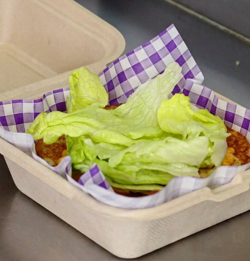 Foglie di lattuga fresca impilate sul pane con salsa rossa in una carta a quadretti viola.