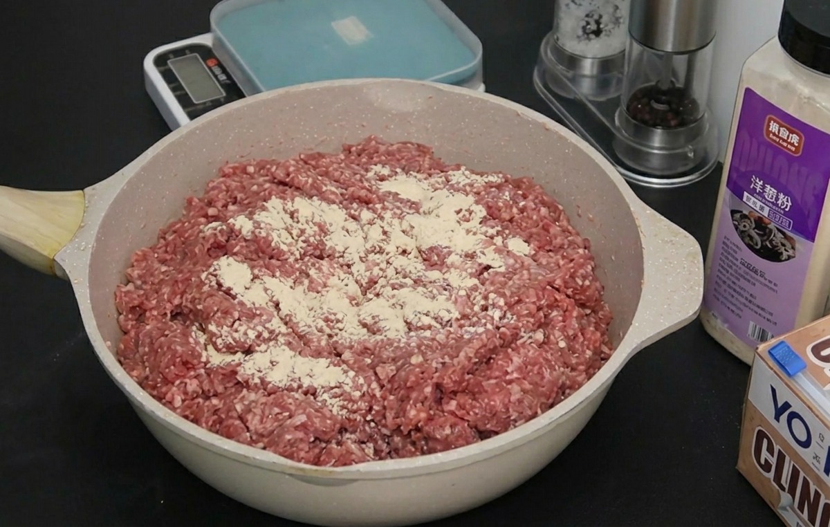 Carne macinata cruda in una pirofila con un sottile strato di cipolla e aglio in polvere in superficie.