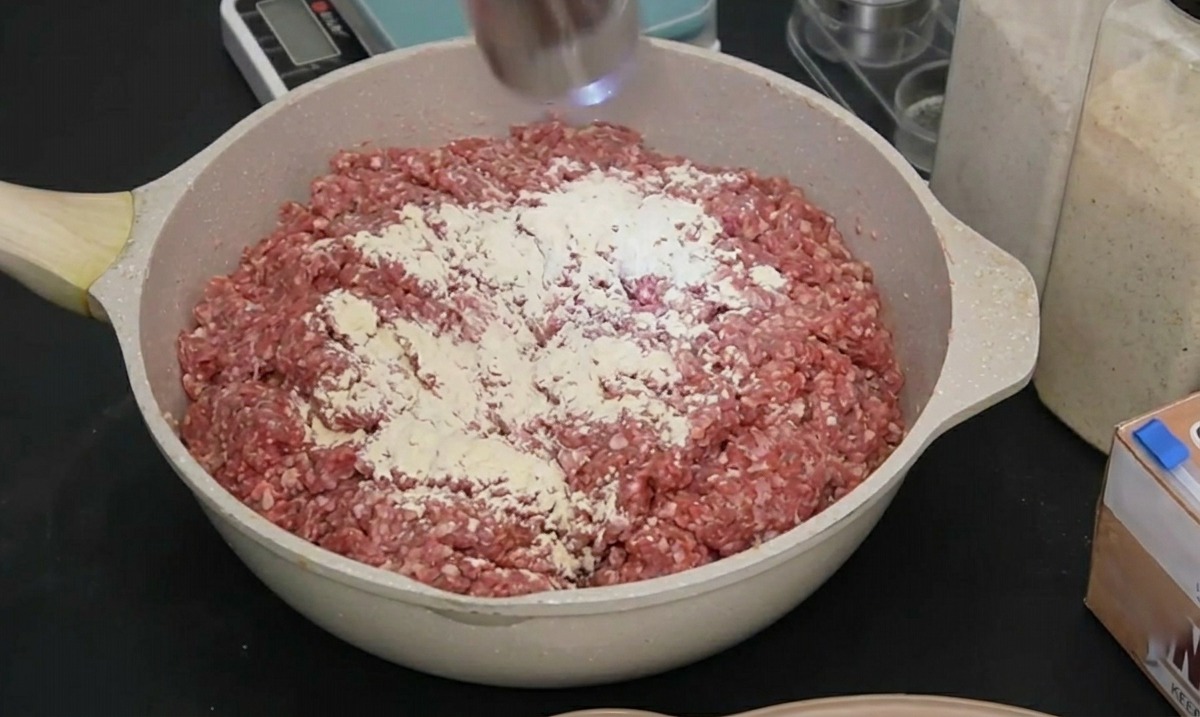 Un macinaspezie elettrico in acciaio inossidabile che macina pepe nero su carne cruda condita in una pirofila.