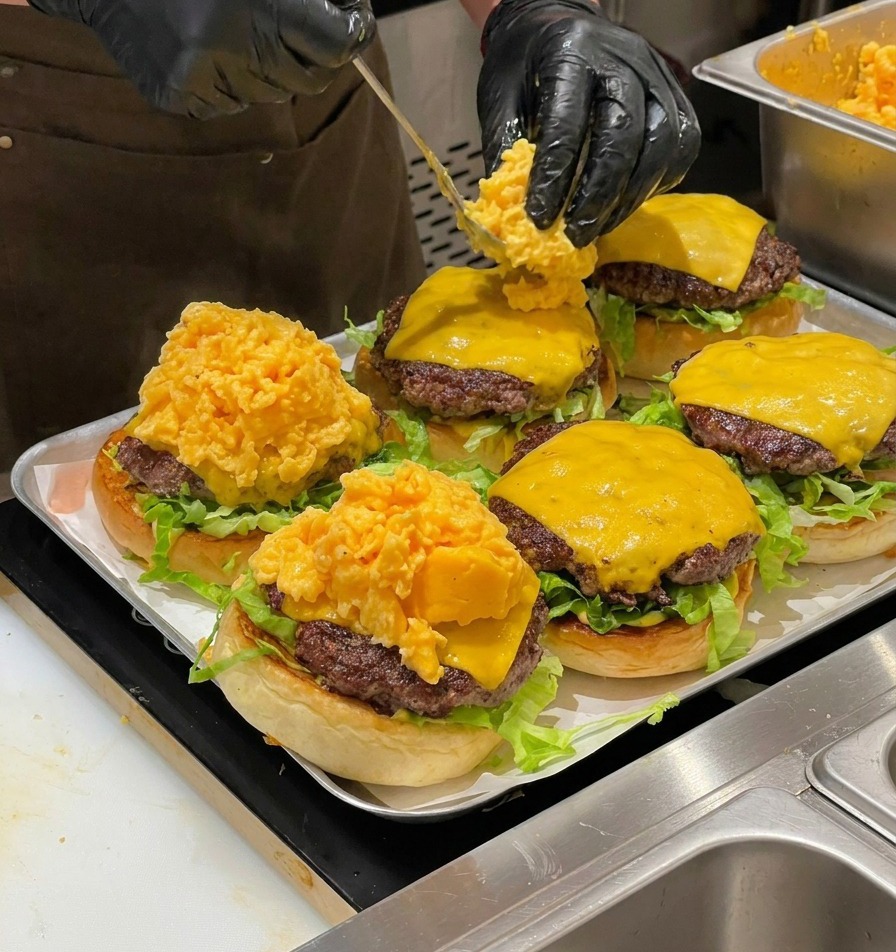 Uno chef che usa un cucchiaio per posizionare una grande porzione di uova strapazzate morbide sui cheeseburger.