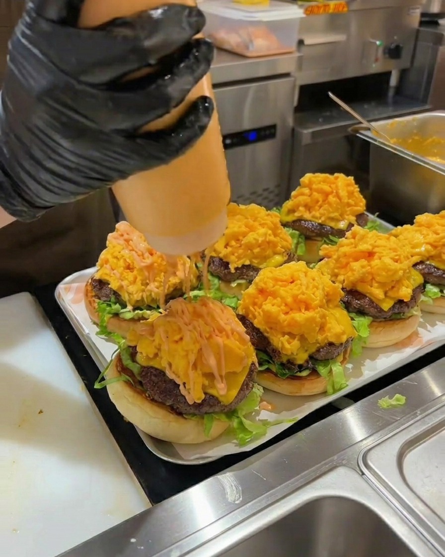 Salsa per hamburger arancione spremuta su unalta pila di uova strapazzate in un hamburger assemblato.