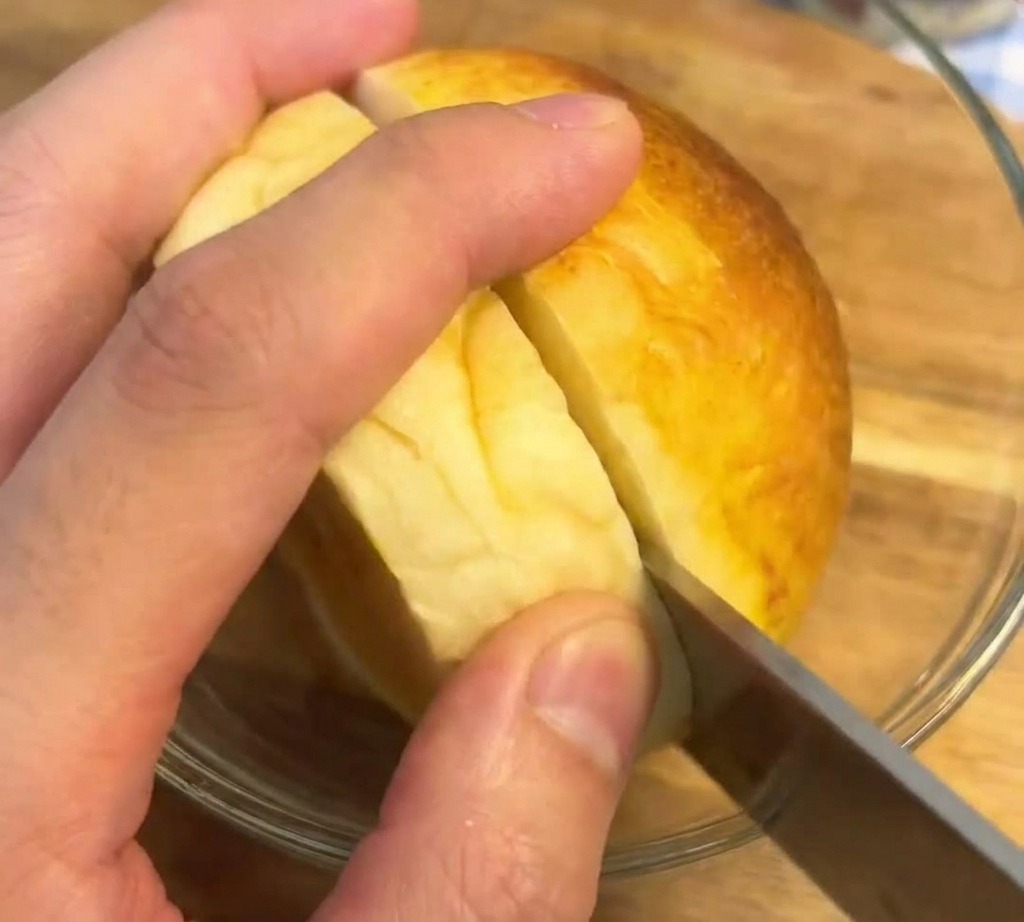 Un coltello seghettato che taglia a metà un pane brioche dorato e tostato su una superficie di legno.