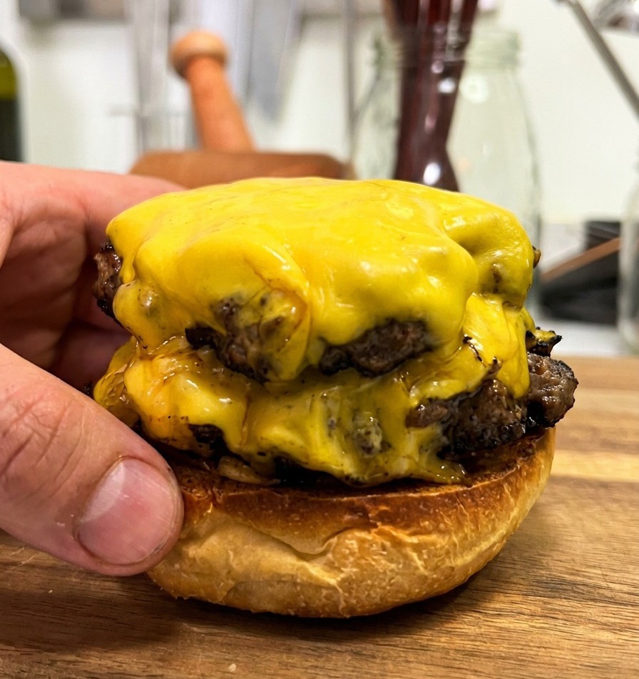 Due patty di carne con formaggio fuso impilati sulla base di un pane tostato.