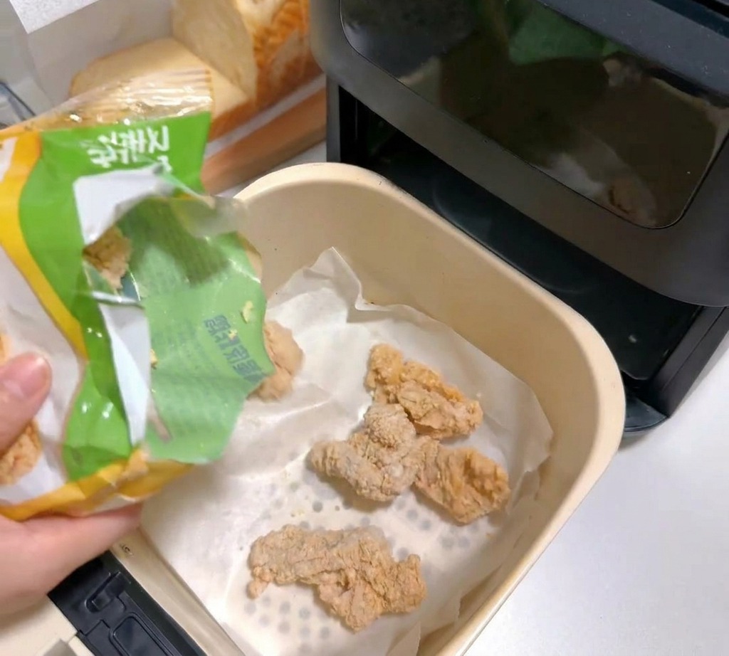 Pezzi di pollo impanato surgelati versati nel cestello della friggitrice ad aria foderato con carta forno.