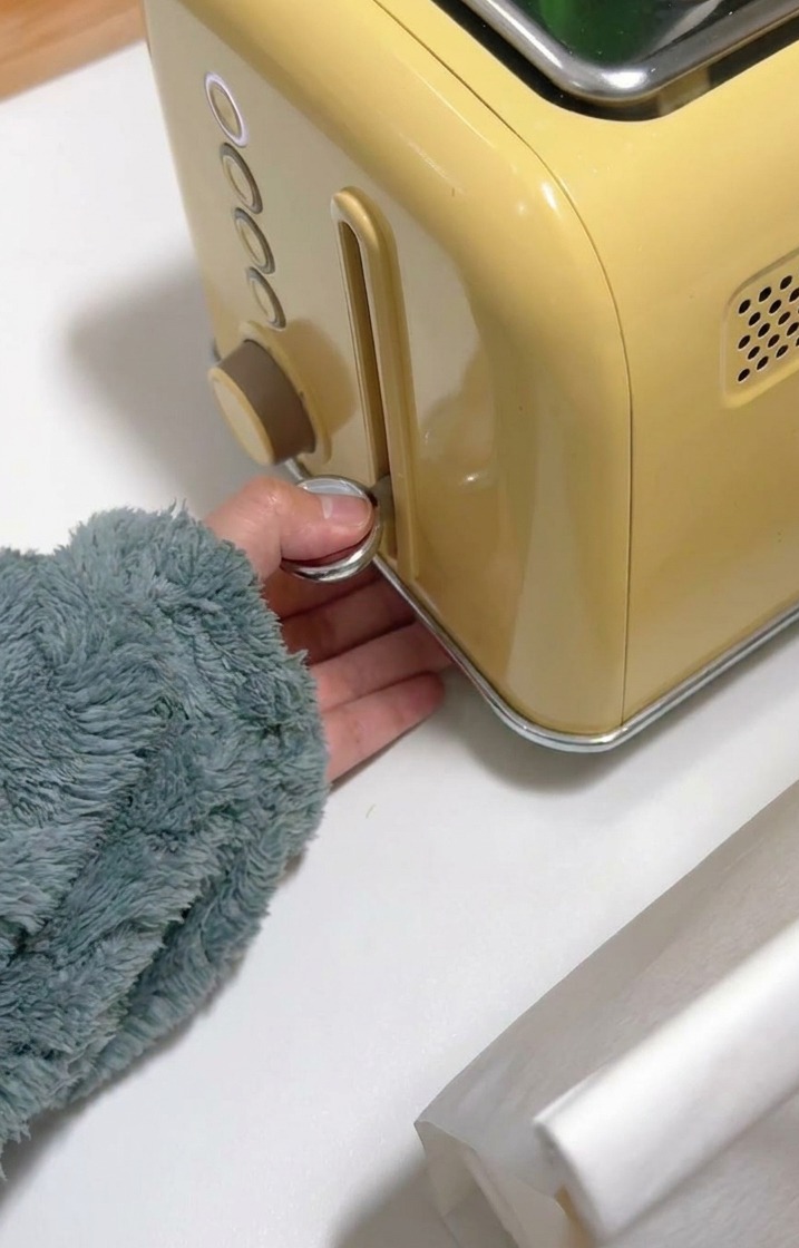 Una mano che abbassa la leva cromata di un tostapane giallo per iniziare a dorare il pane.