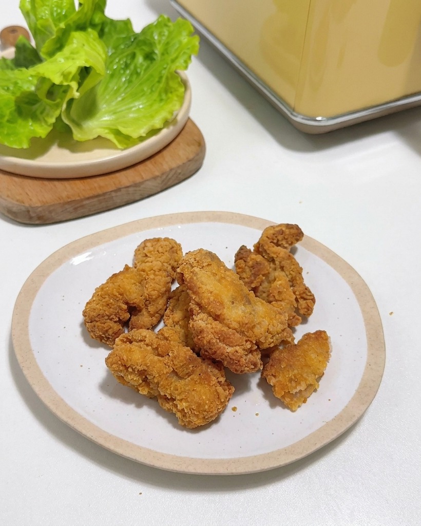 Pezzi di pollo fritto croccante su un piatto bianco accanto a foglie di lattuga fresca.