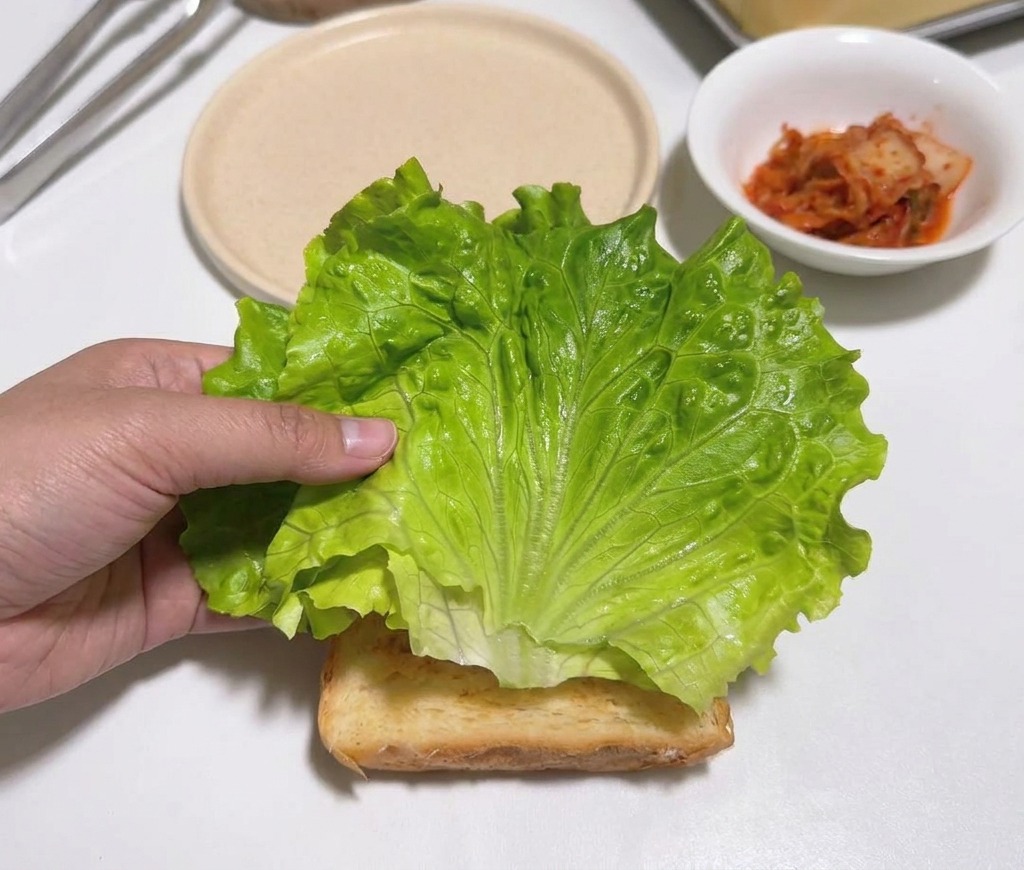Una mano che posiziona una foglia di lattuga verde su una fetta di pane tostato.