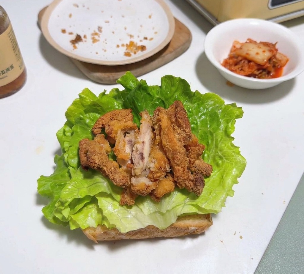 Pezzi di pollo fritto stratificati sopra una foglia di lattuga e pane tostato.