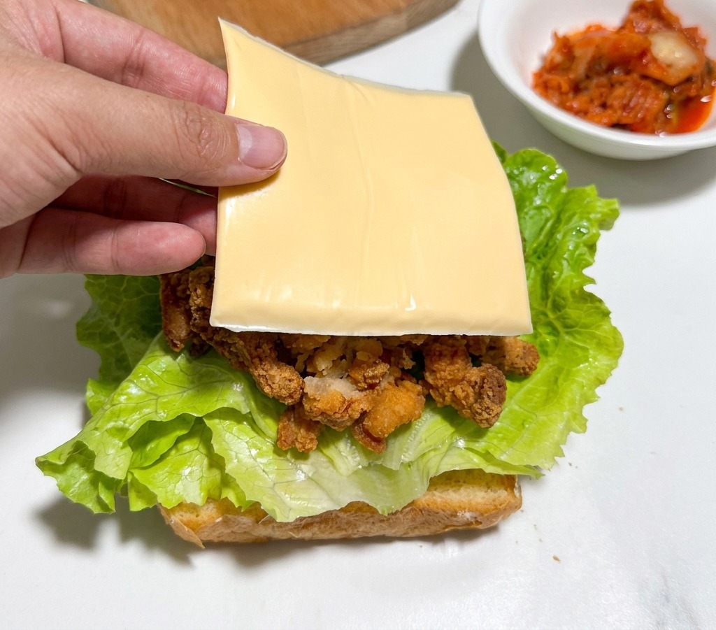 Una mano che posiziona una fetta di formaggio giallo sul pollo fritto stratificato sopra la lattuga.