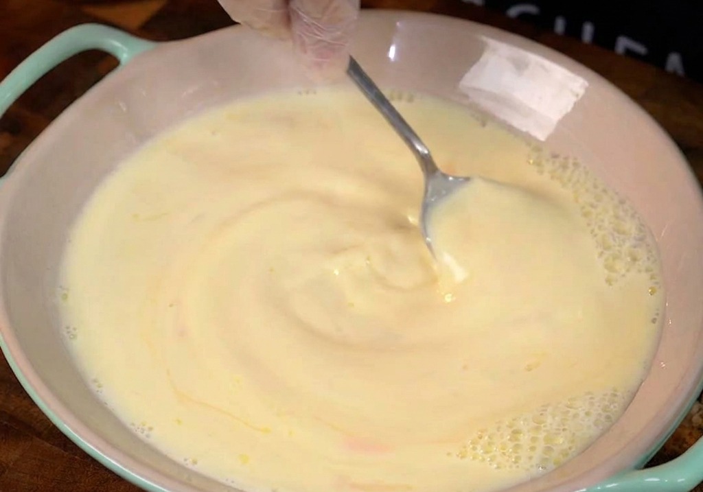 Latte e uova con venature di miele mescolati in una ciotola di ceramica rosa.