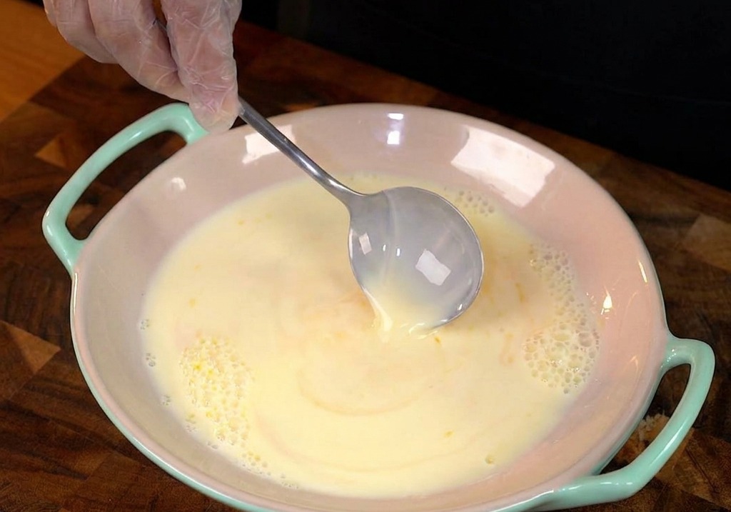 Una fetta spessa di pane bianco immersa in una ciotola con la pastella di uova e latte.