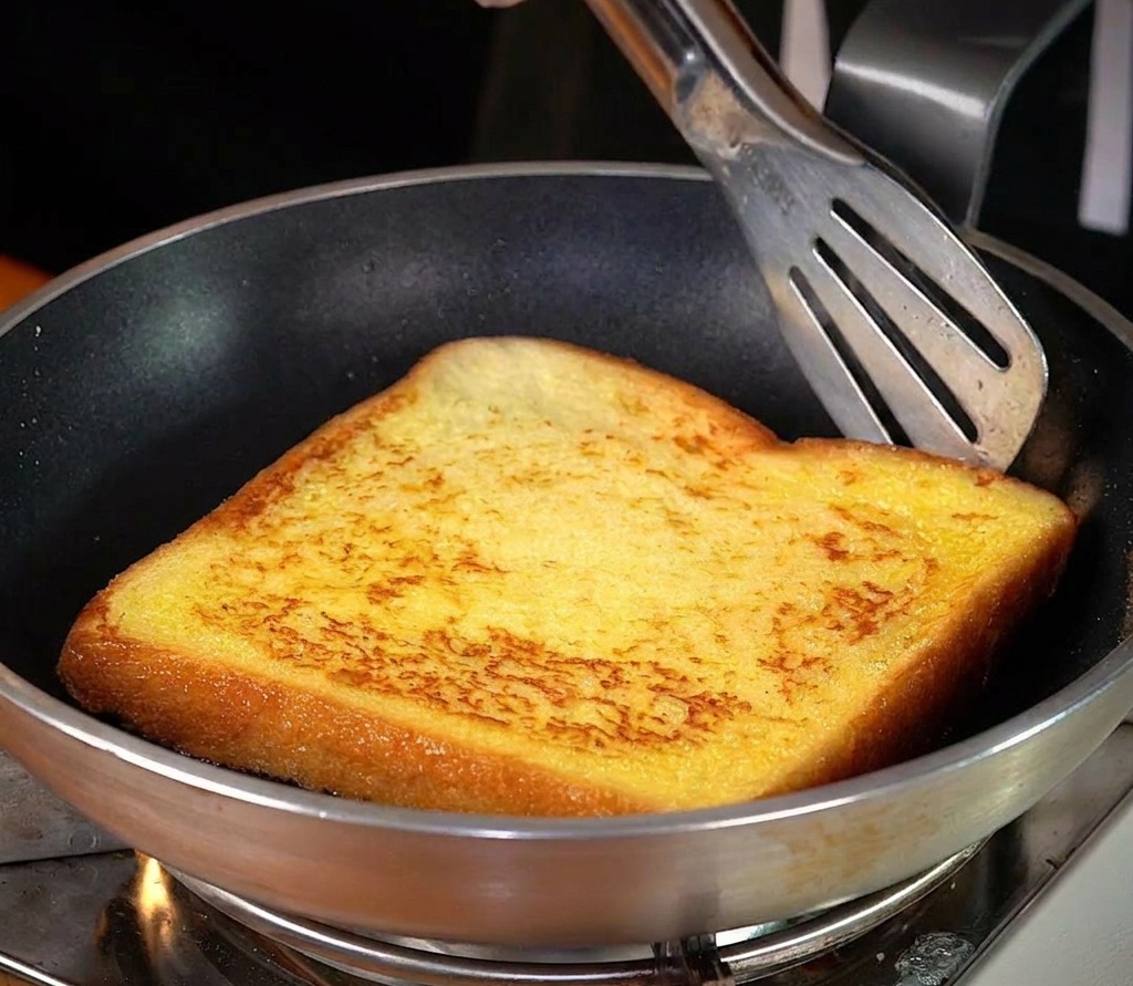 Una fetta di pane in padella con burro fuso che mostra una crosticina dorata vibrante.