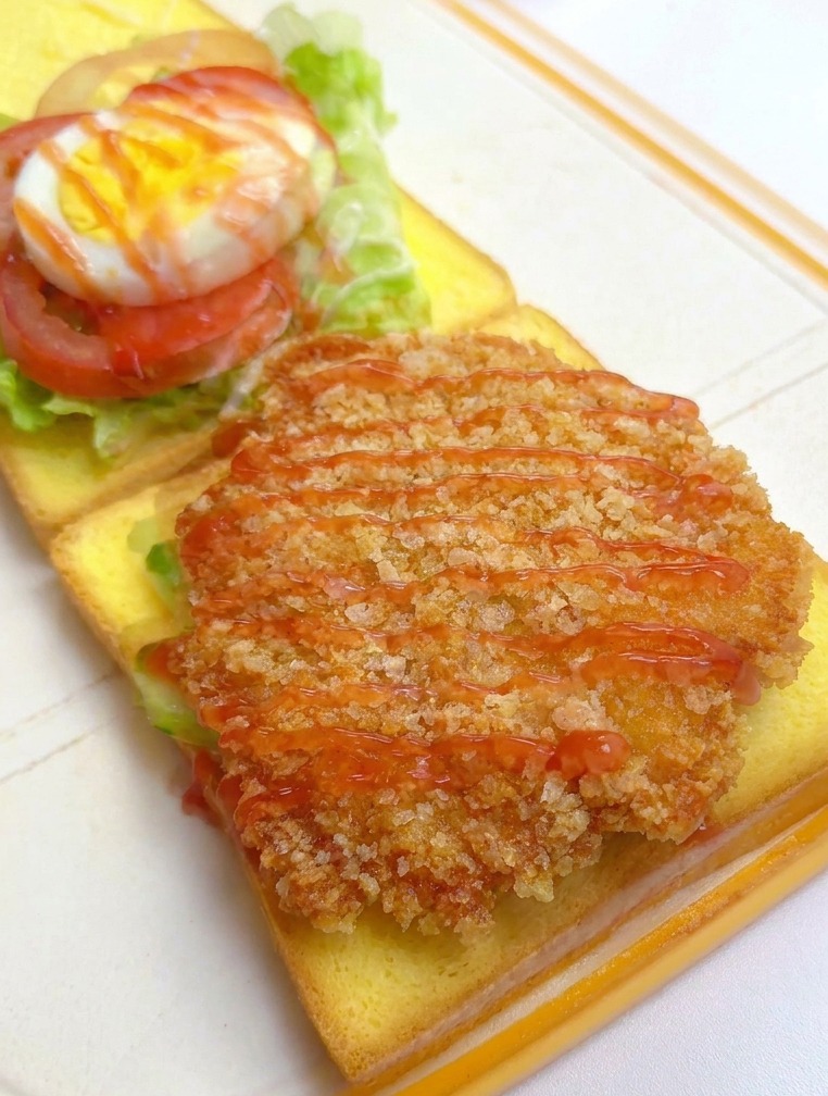 Un filetto di pollo dorato sul pane viene condito con ketchup, con gli altri strati visibili sullo sfondo.