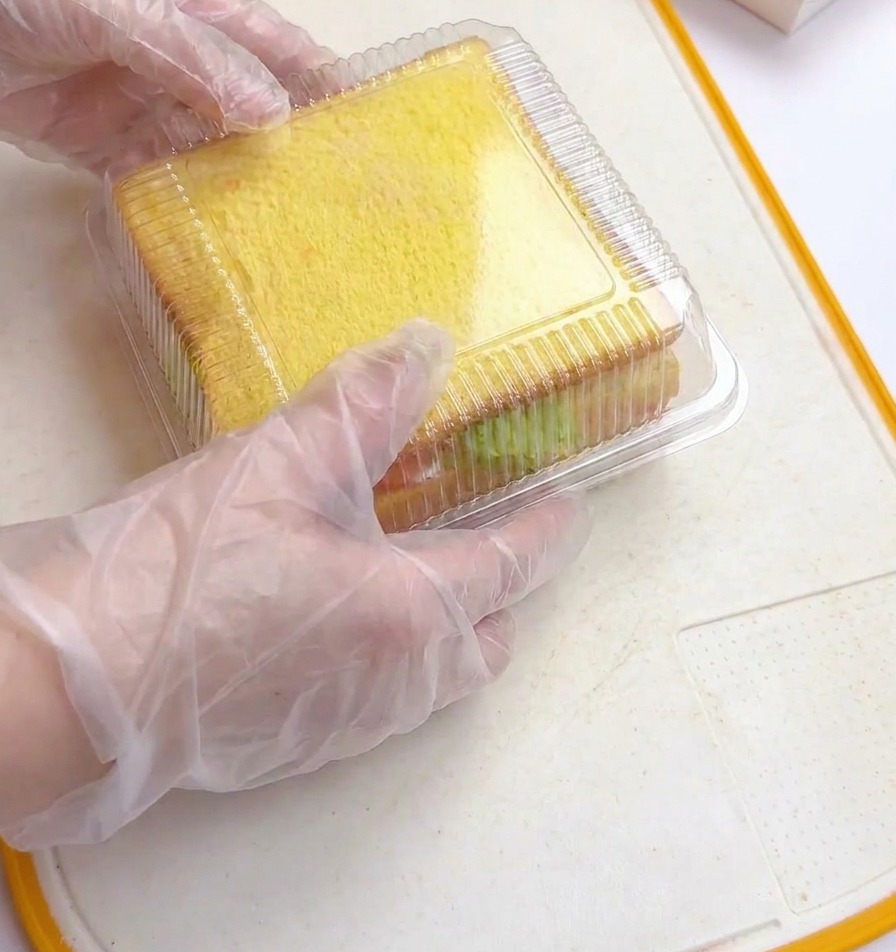 Mani con guanti di plastica che premono il coperchio trasparente di uno stampo su un sandwich spesso e stratificato.