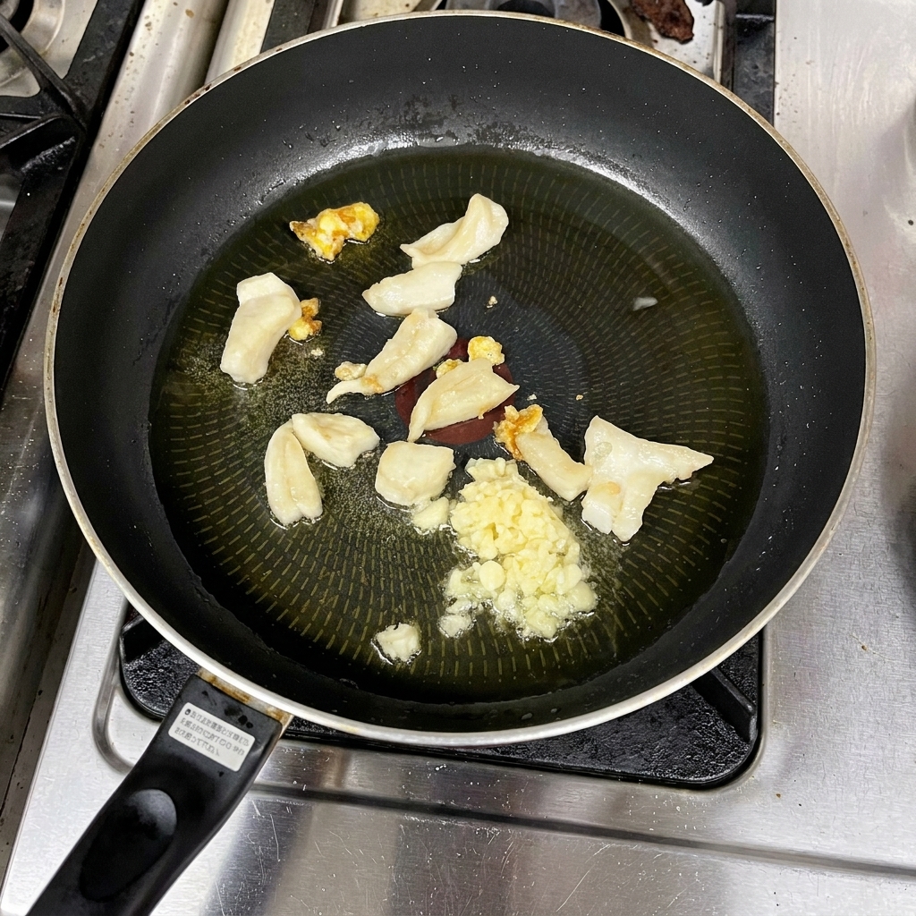 Aglio tritato che soffrigge nel grasso sciolto e trasparente in una padella.