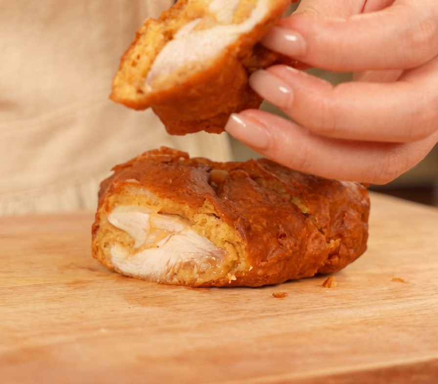 Un pezzo di pollo fritto tagliato su un tagliere in legno che mostra la carne succosa e la crosta dorata.