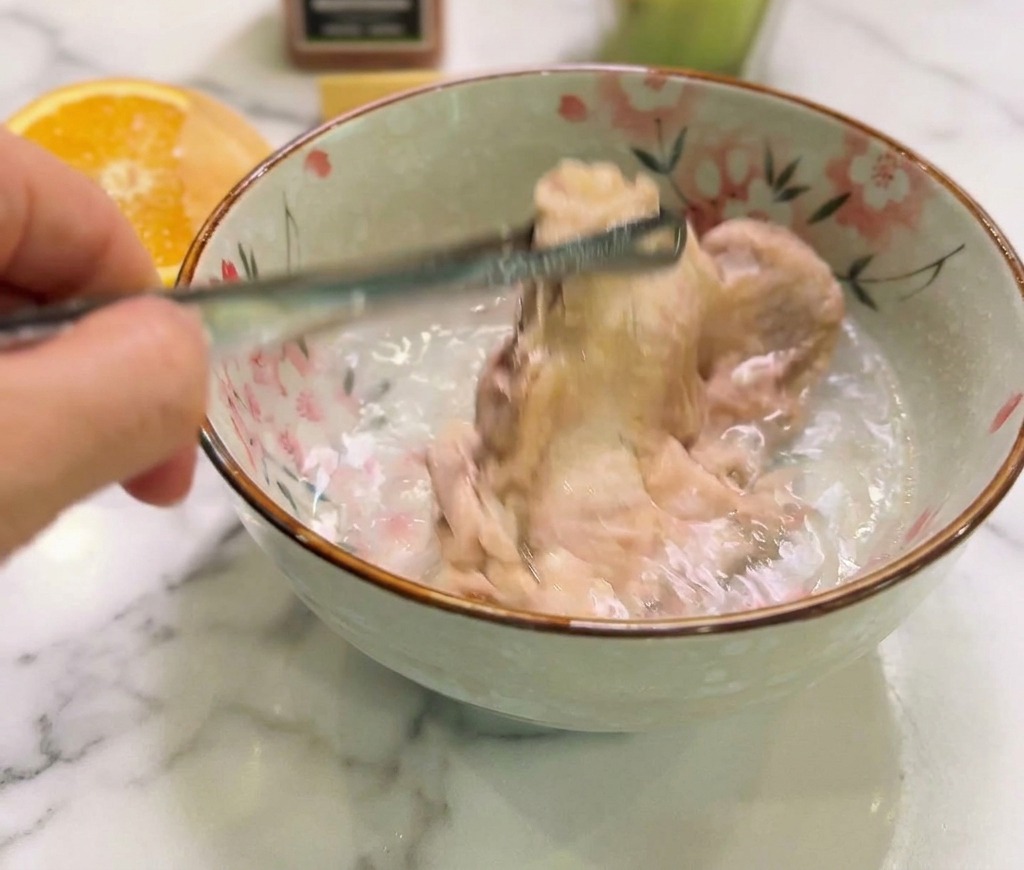 Pollo cotto appena tolto dal fuoco immerso in una ciotola di ceramica con acqua fredda pulita.