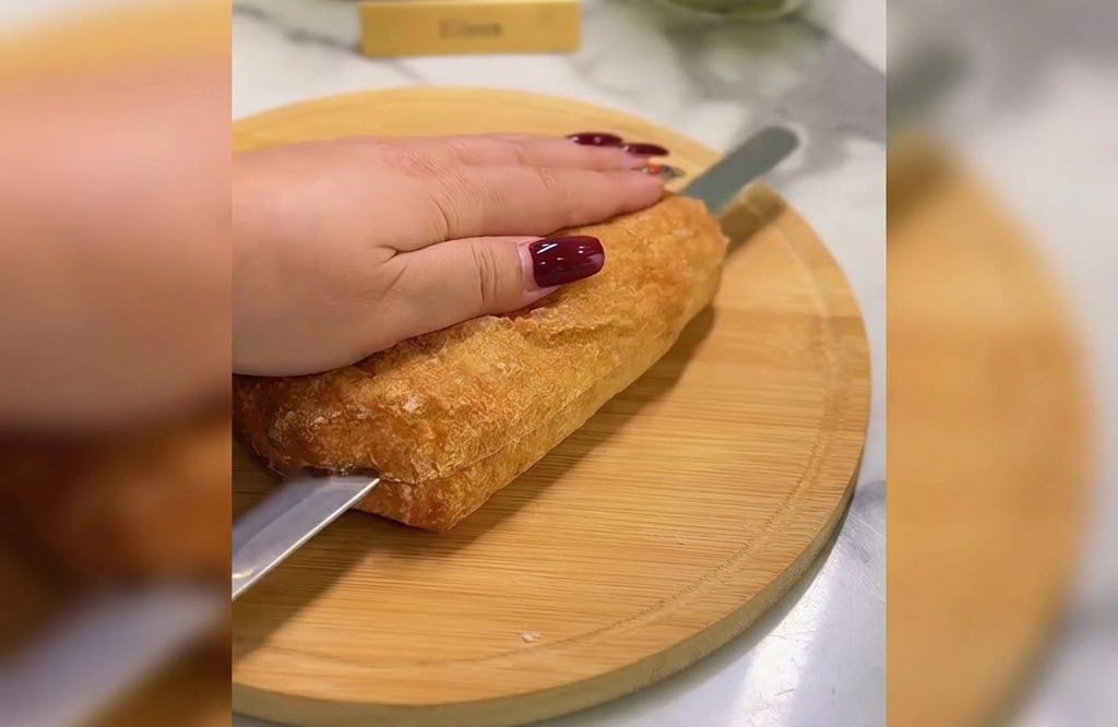 Mano che tiene una ciabatta dorata mentre un coltello seghettato la taglia a metà su un tagliere.