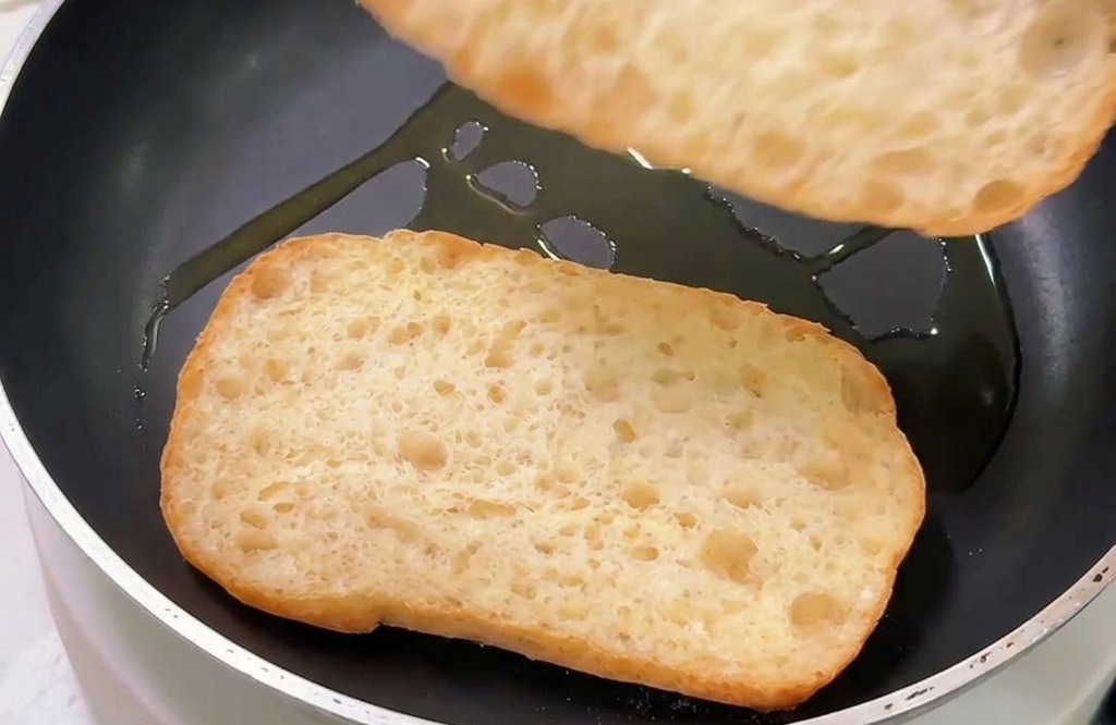 Due metà di ciabatta tostate dal lato del taglio in una padella antiaderente con un filo dolio.