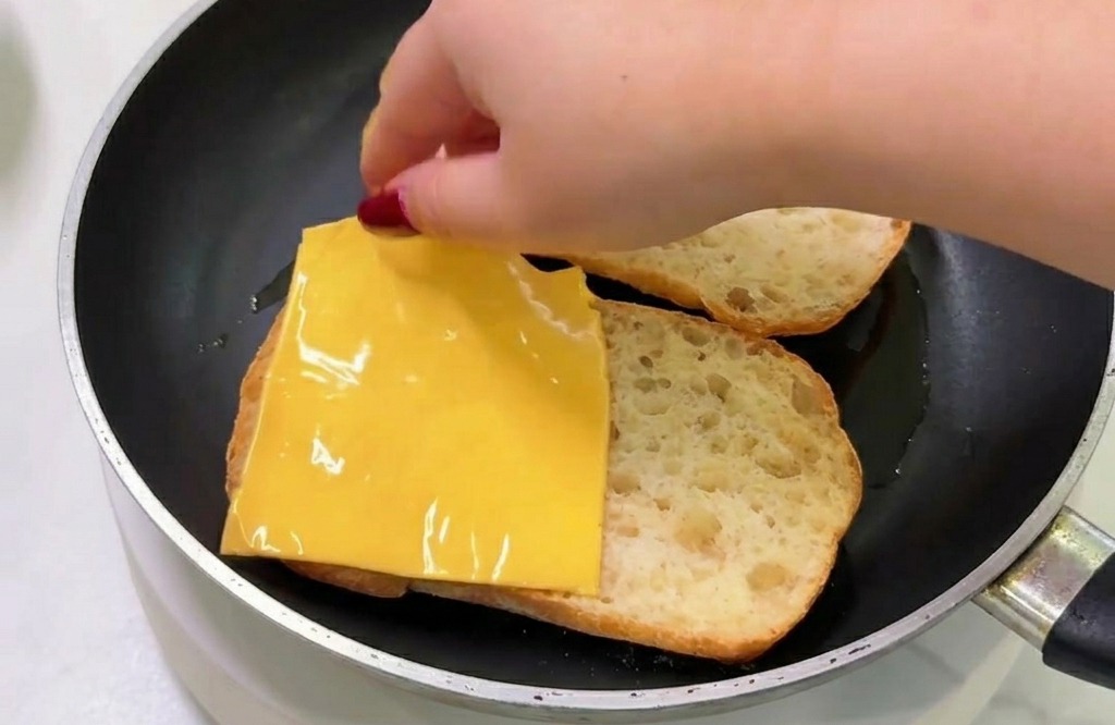 Mano che mette una fetta quadrata di formaggio sul pane tostato allinterno di una padella calda.