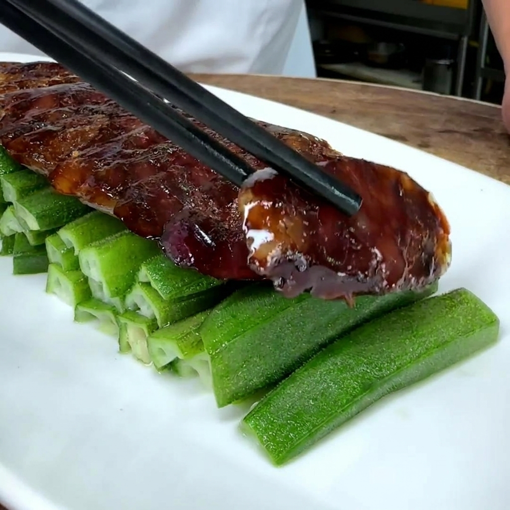 Primo piano di rondelle di salsiccia cinese disposte su un letto di okra verde in un piatto bianco.