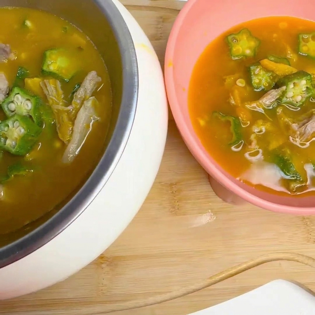 Un mestolo che mescola delicatamente una zuppa in ebollizione contenente pezzi di okra e anatra in una pentola.