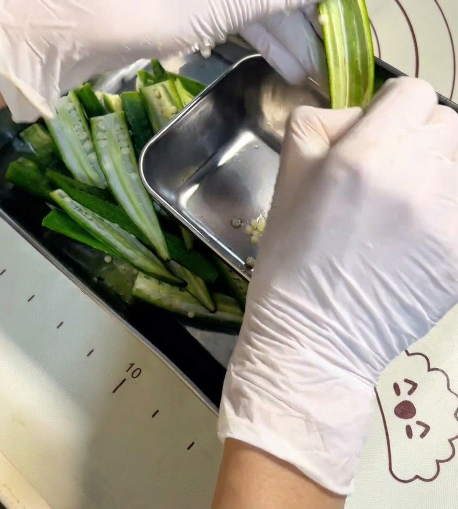 Una mano usa un cucchiaino per pulire i semi da un baccello di okra aperto.