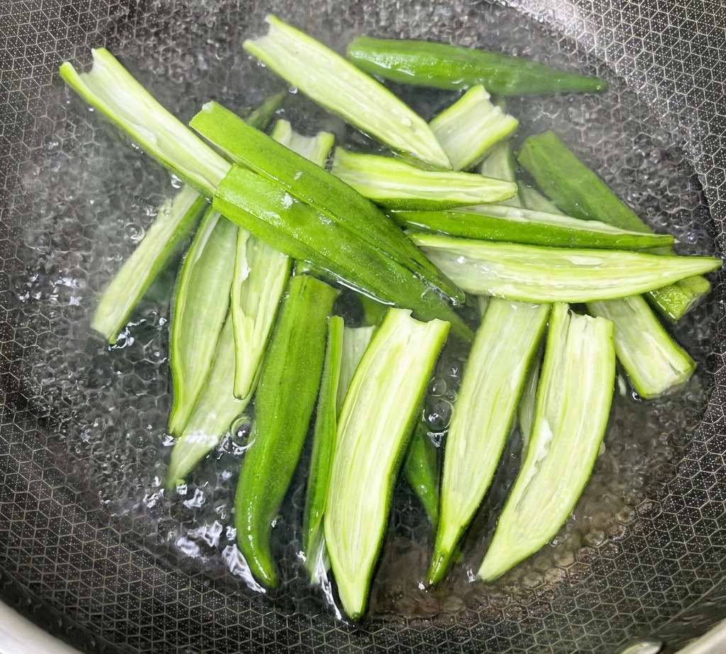 Baccelli di okra aperti che bollono in una pentola dacqua sul fornello.