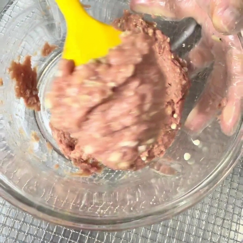 Carne macinata di anatra e semi di gombo mescolati in una ciotola con una spatola in silicone gialla.